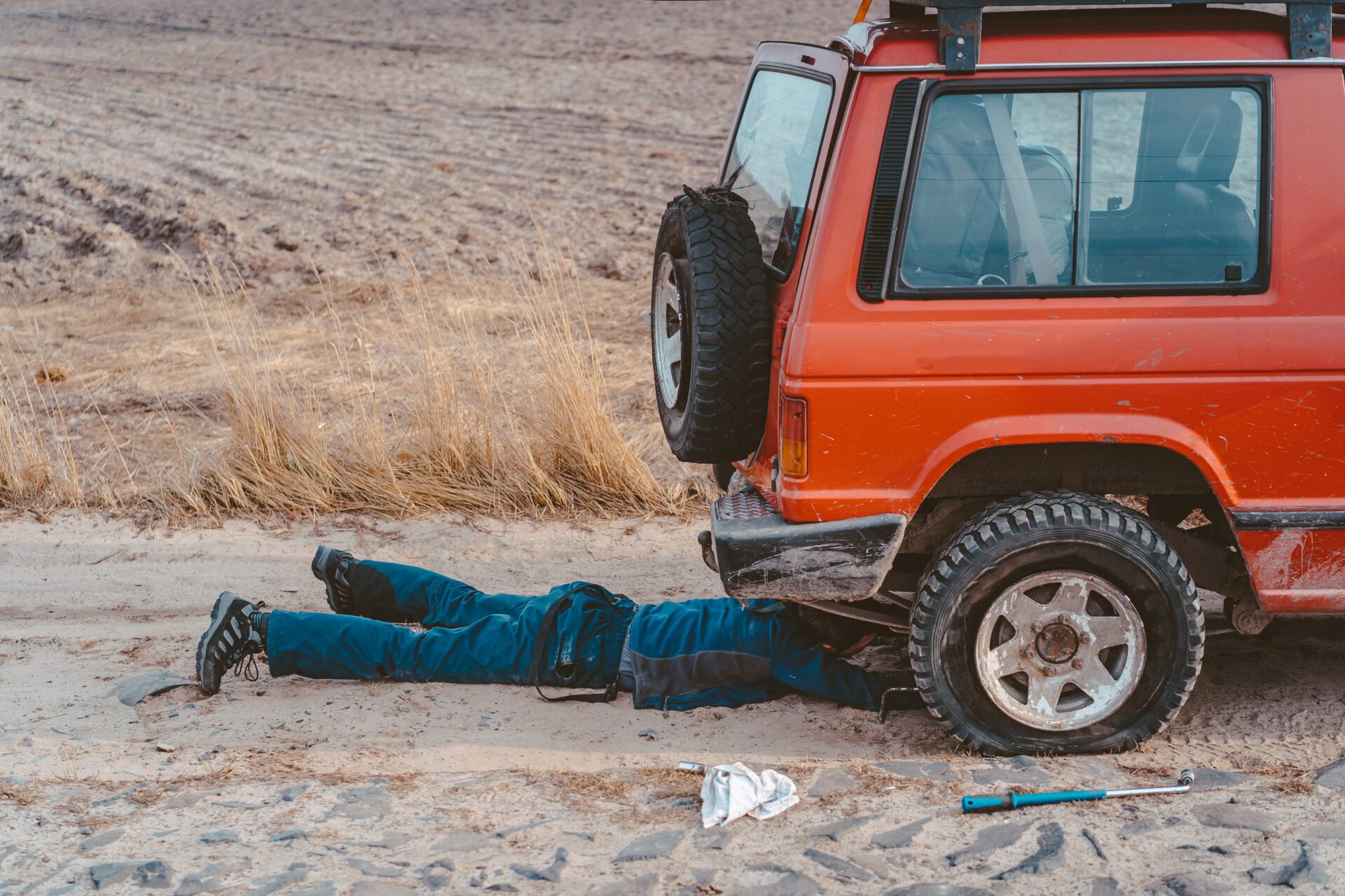 man lies under a 4x4 car on a dirt road Truck Jackknifing